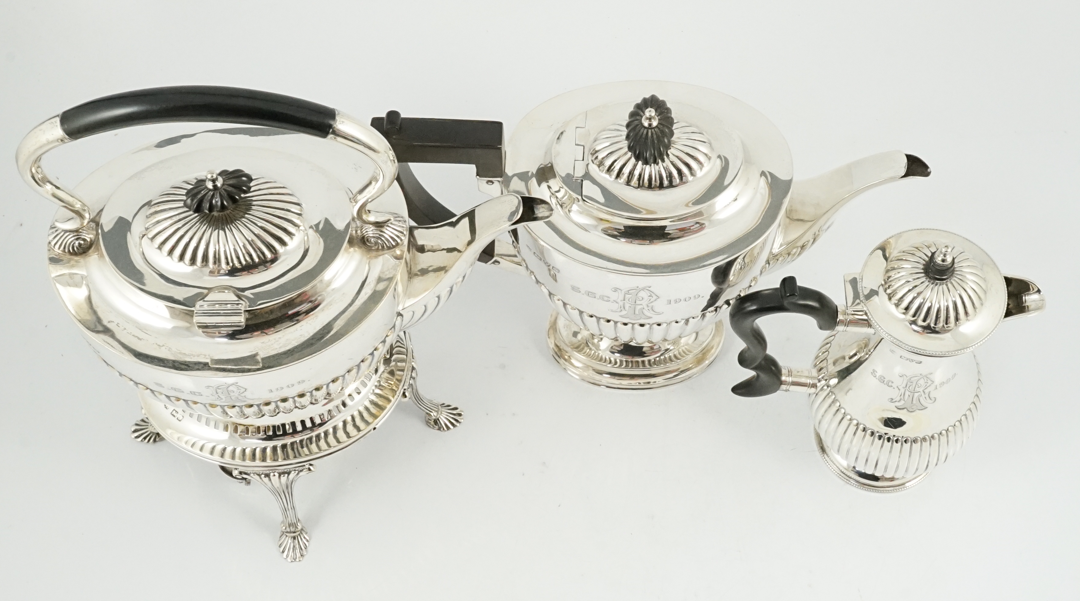 An Edwardian demi-fluted silver tea kettle on stand with burner, with matching pedestal coffee pot and hot water pot, by Barker Brothers